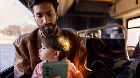 A South Asian man holding his child while they ride on public transportation