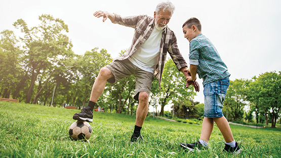 An older man plays soccer with a pre-teen boy