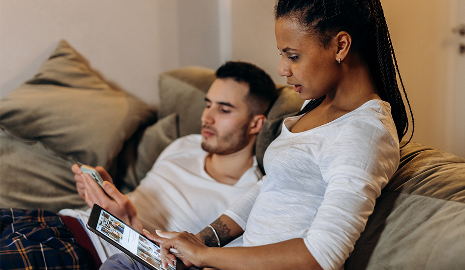 Couple sitting on sofa looking at their smart devices