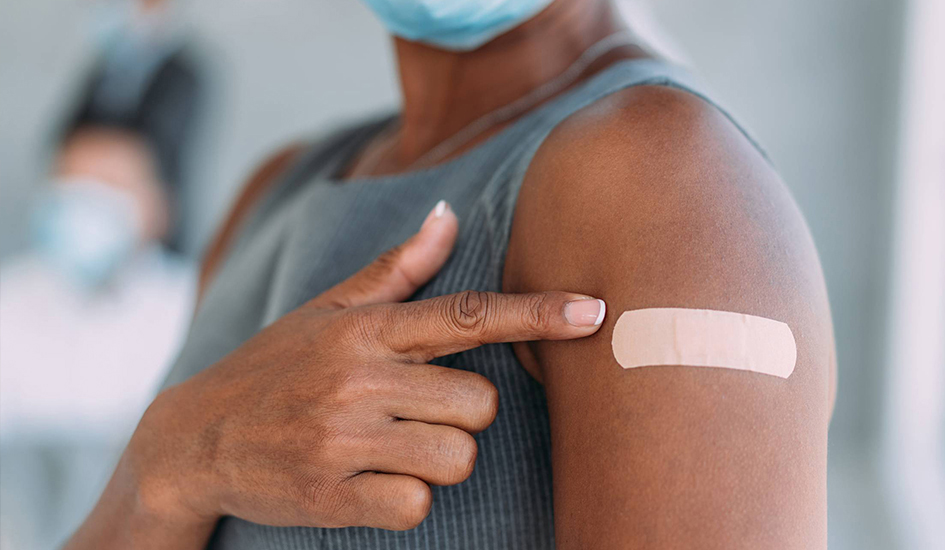 Photo of woman pointing to bandaid on arm after vaccination